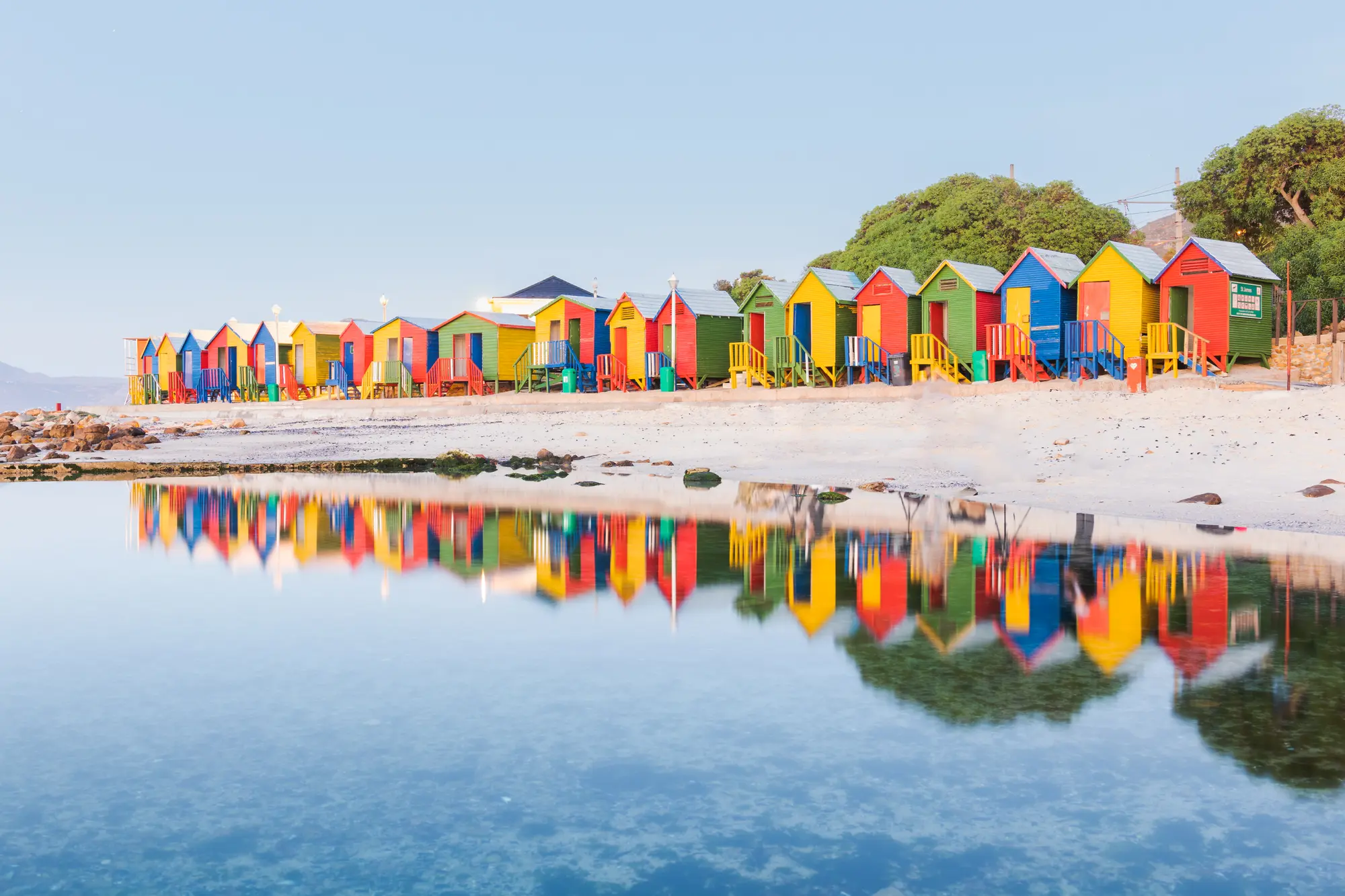 The colourful St James beach huts mirrored in the still water of an early morning high tide