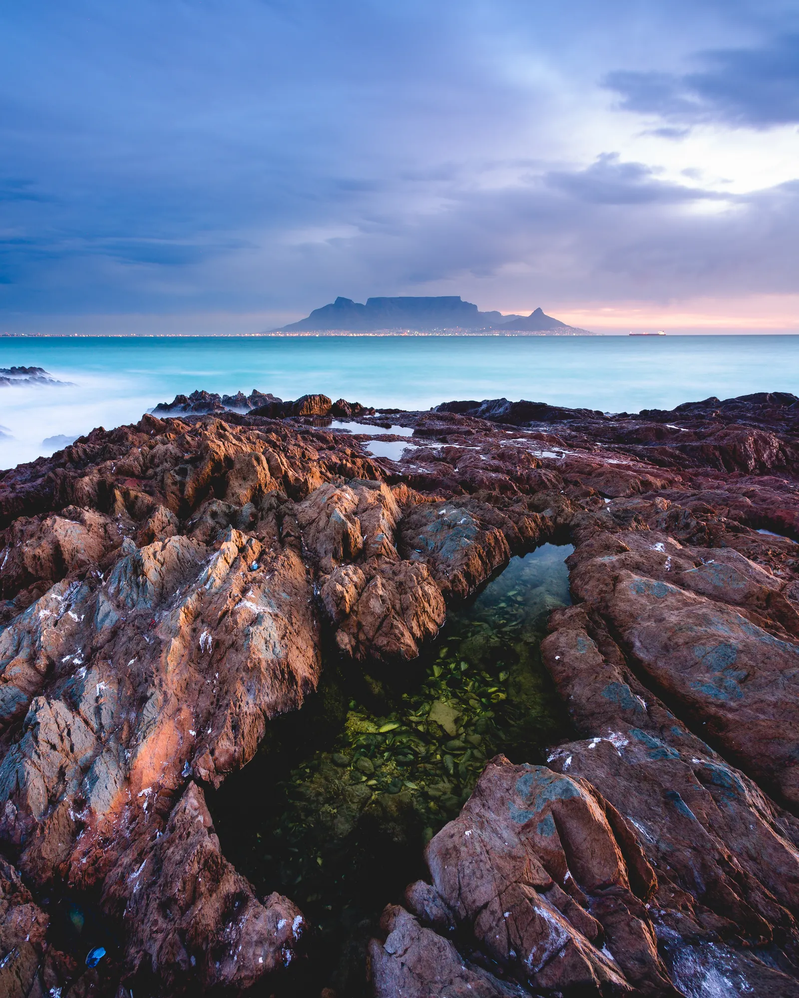Storm light in deep blues over Table Bay, Table Mountain across the water and a rock pool in the foreground