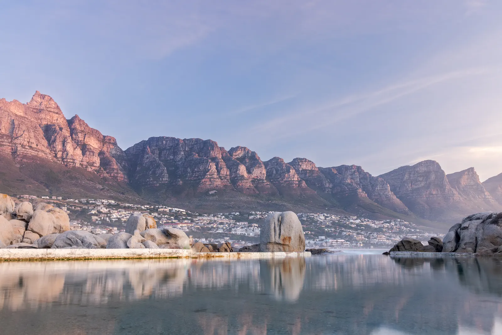 The Twelve Apostles reflected in the glassy tidal pool at Maiden's Cove at first light, granite boulders catching early sun